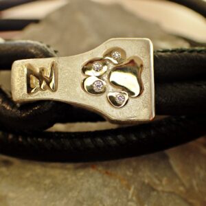 Wickelarmband aus schwarzem Nappaleder mit silberner Schnalle mit Hundepfote, goldener Belötung und Brillianten.